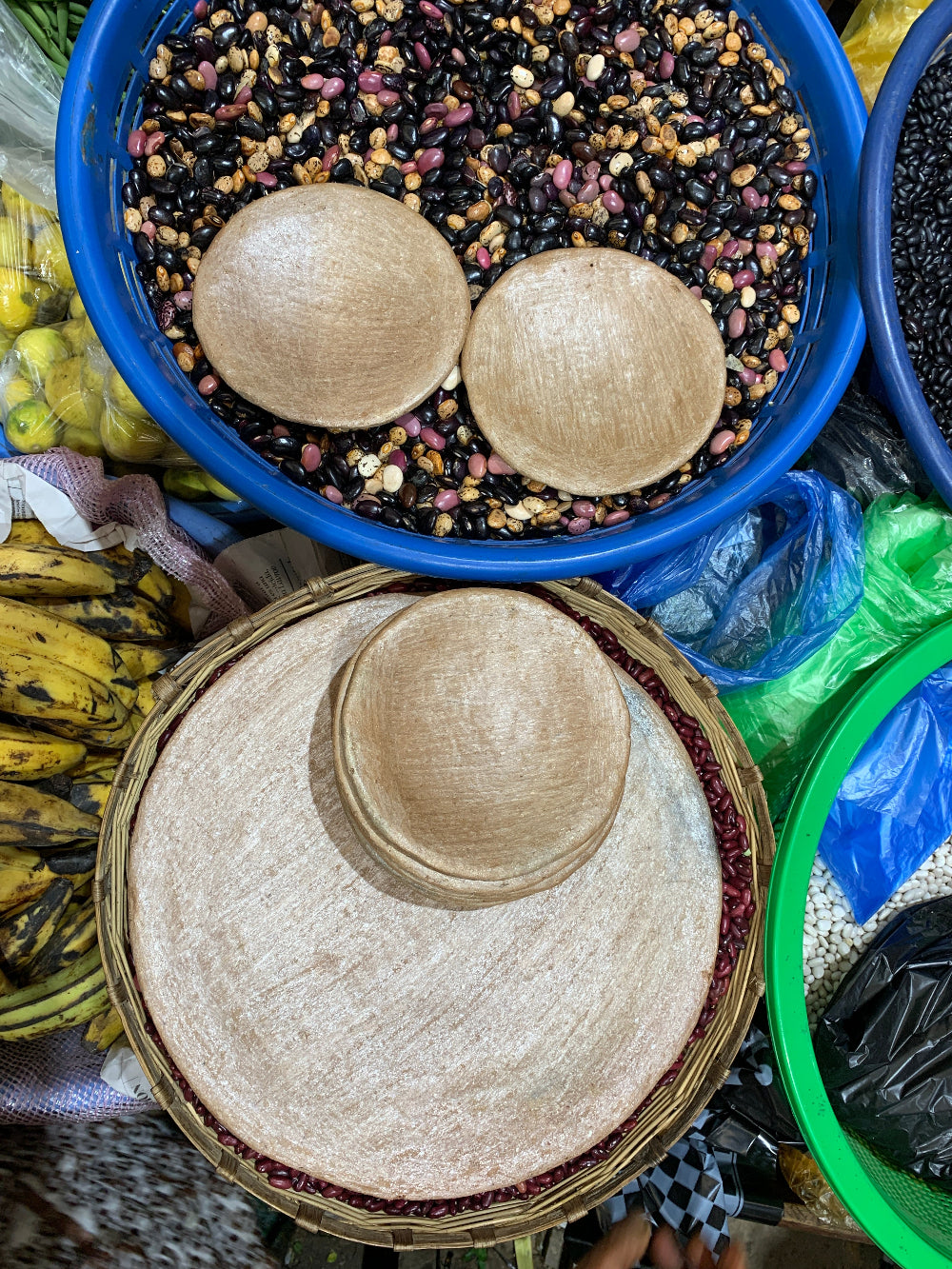 Baskets full of beans and other fresh produce at the market, with terra cotta comal plates 