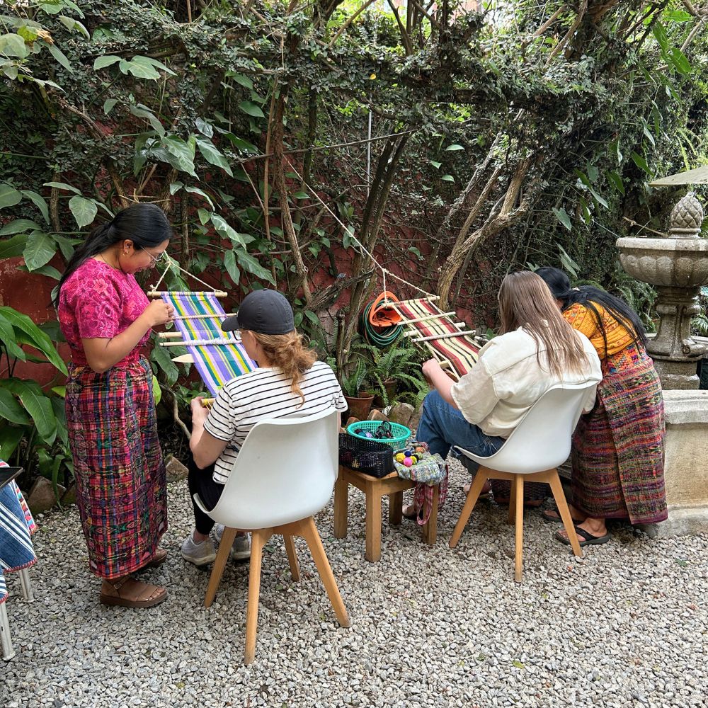 Two students with their respective teachers in the Kakaw Designs garden, enjoying the weaving class.