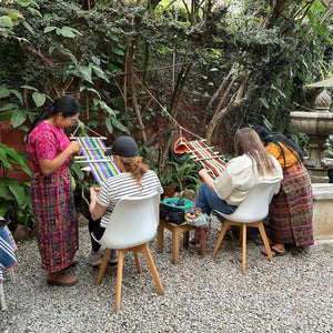 Two students with their respective teachers in the Kakaw Designs garden, enjoying the weaving class.