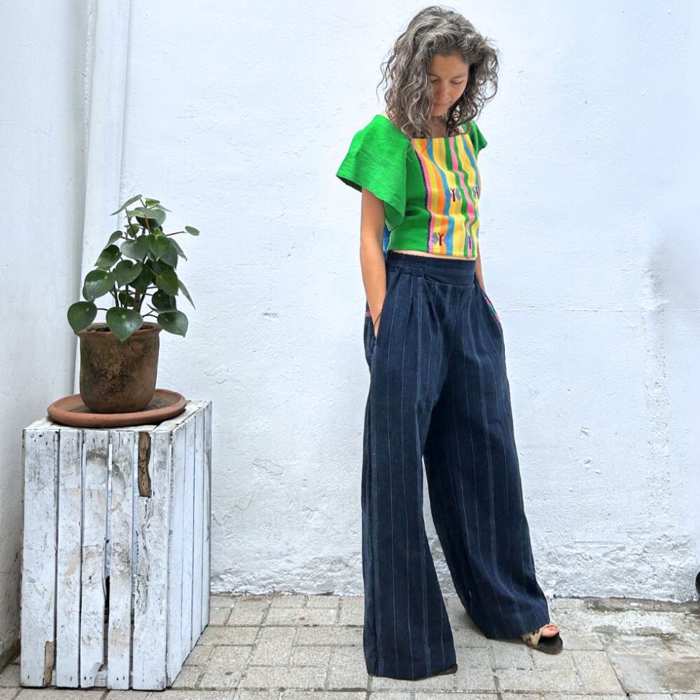 A person wearing a colorful top with vertical stripes paired with Navy pinstripe corte trousers with thin colorful randa on the side.