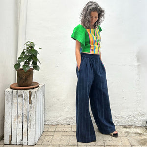 A person wearing a colorful top with vertical stripes paired with Navy pinstripe corte trousers with thin colorful randa on the side.