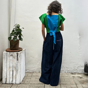 A person wearing a colorful top with vertical stripes paired with Navy pinstripe corte trousers with thin colorful randa on one back pocket.