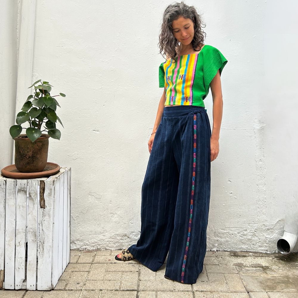 A person wearing a colorful top with vertical stripes paired with Navy pinstripe corte trousers with thin colorful randa on the side.