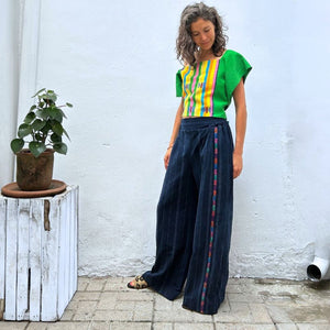 A person wearing a colorful top with vertical stripes paired with Navy pinstripe corte trousers with thin colorful randa on the side.