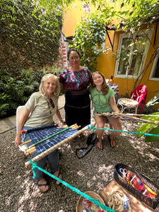 Mother and daughter pair weaving together in a lush courtyard
