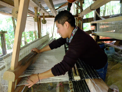 Person operating a traditional weaving loom in an outdoor setting