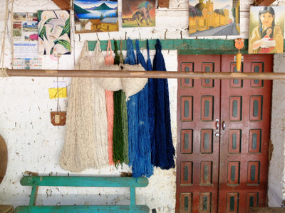 Colorful yarn hanging on a rack with a wooden door and wall art in the background