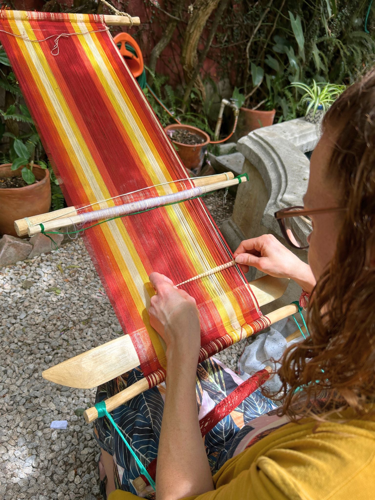 A student beginning to weave brocade patterns on the loom she created herself, using bright, warm colored threads.