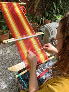 A student beginning to weave brocade patterns on the loom she created herself, using bright, warm colored threads.