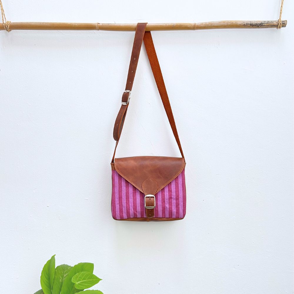 Pink striped bag with brown leather strap and accents hanging on a white wall.