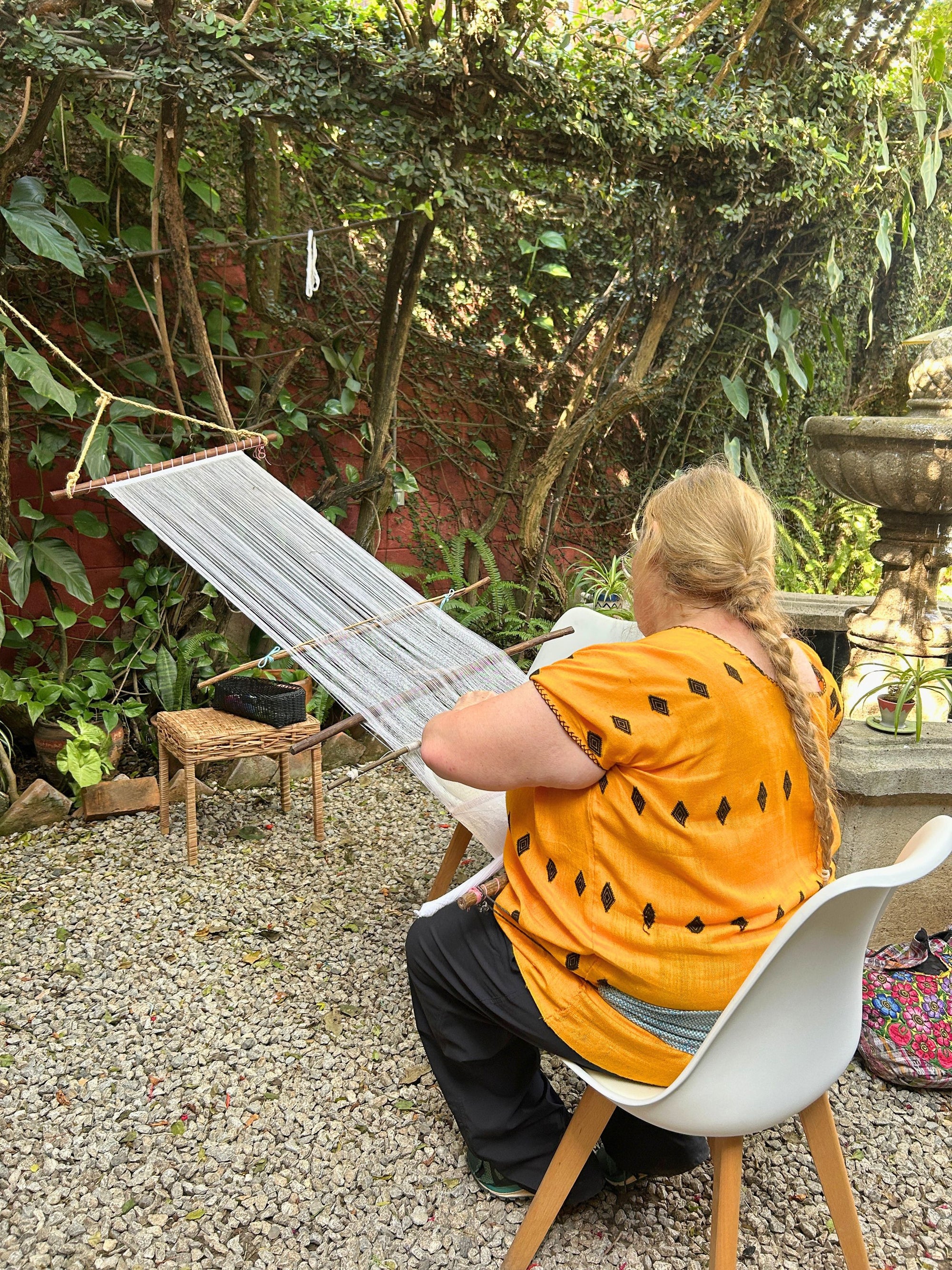 A student weaving on a backstrap loom in the Kakaw Designs garden.