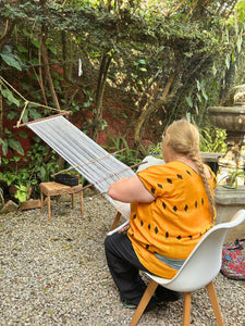 A student weaving on a backstrap loom in the Kakaw Designs garden.