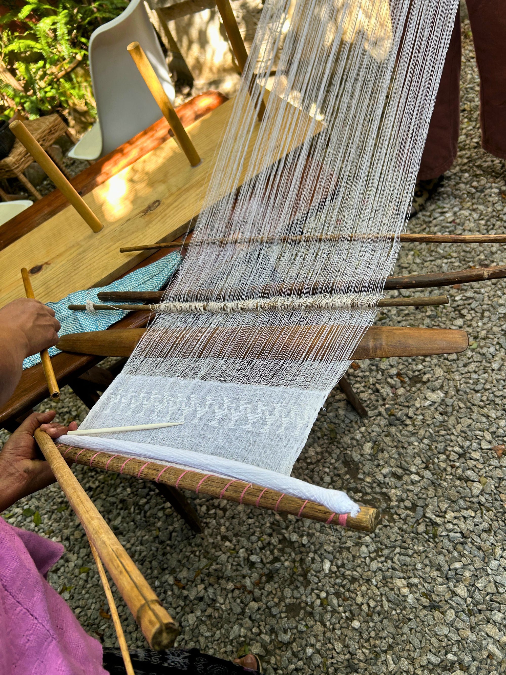 A backstrap loom prepared with white threads for the traditional Pikbil weaving technique from Cobán, showing both the completed woven section and the portion still in progress.