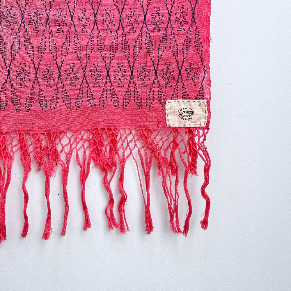 Close-up of a pink cochienal scarf with indigo blue patterns and fringes on a white background