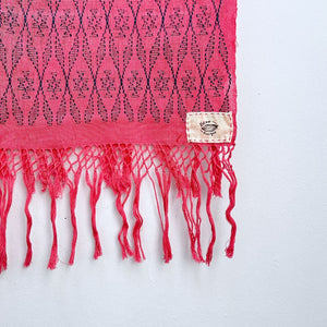 Close-up of a pink cochienal scarf with indigo blue patterns and fringes on a white background