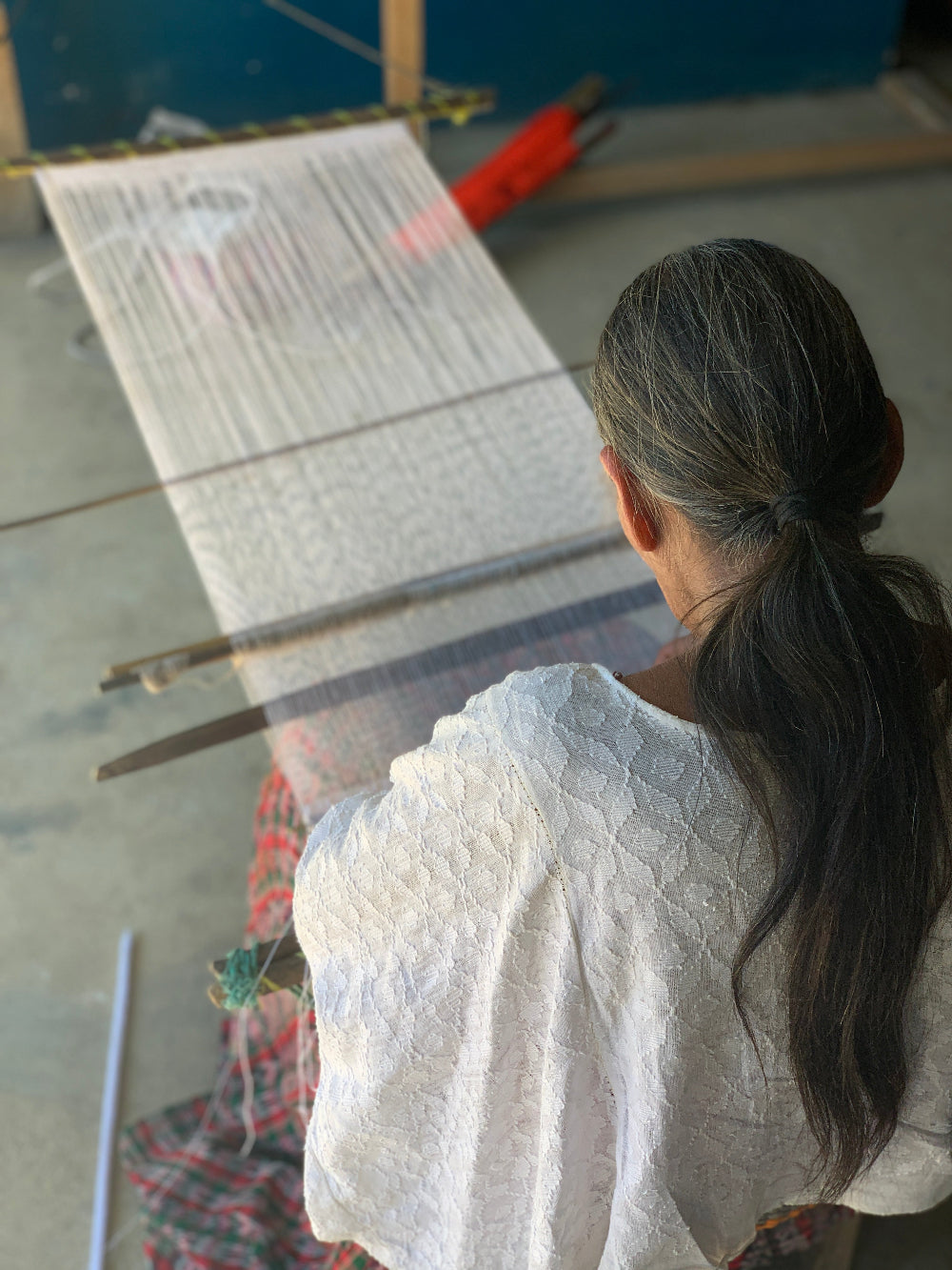 An image of a master weaver on her white pikbil loom from behind.