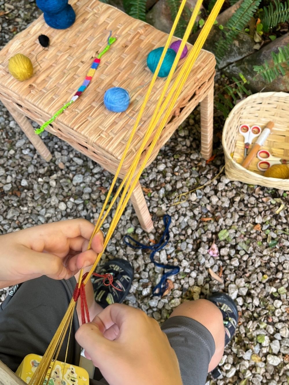 Person holding yellow yarn with a small wooden table and yarn n the background