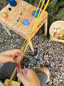 Person holding yellow yarn with a small wooden table and yarn n the background