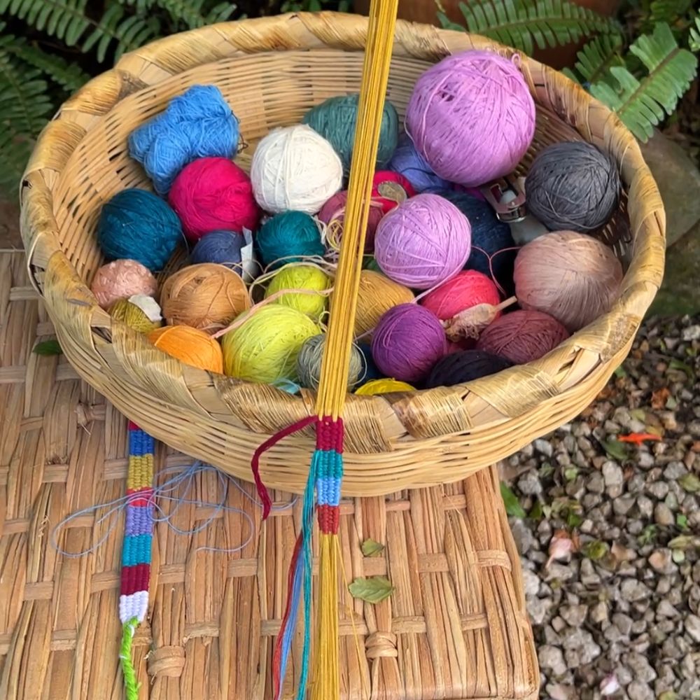 Wicker basket filled with colorful yarn balls and a bracelet being woven in the foreground.