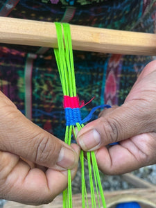 Close-up of hands weaving colorful threads on a loom.