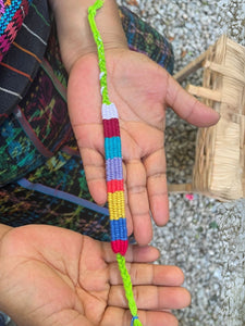 Colorful woven bracelet held between two hands with a textured background