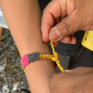 Close-up of a hand tying a colorful bracelet on another person's wrist.