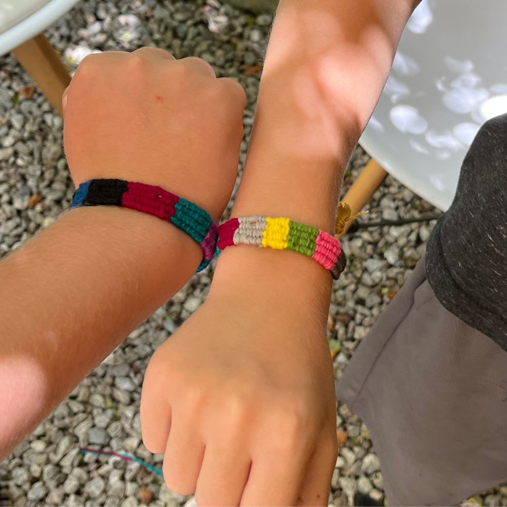 Two children's hands wearing colorful beaded bracelets on a pebbly surface.