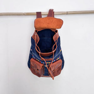 Corte denim backpack with brown leather straps and pockets on a white background