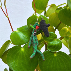 Two quetzal earrings hanging from a plant with green leaves.