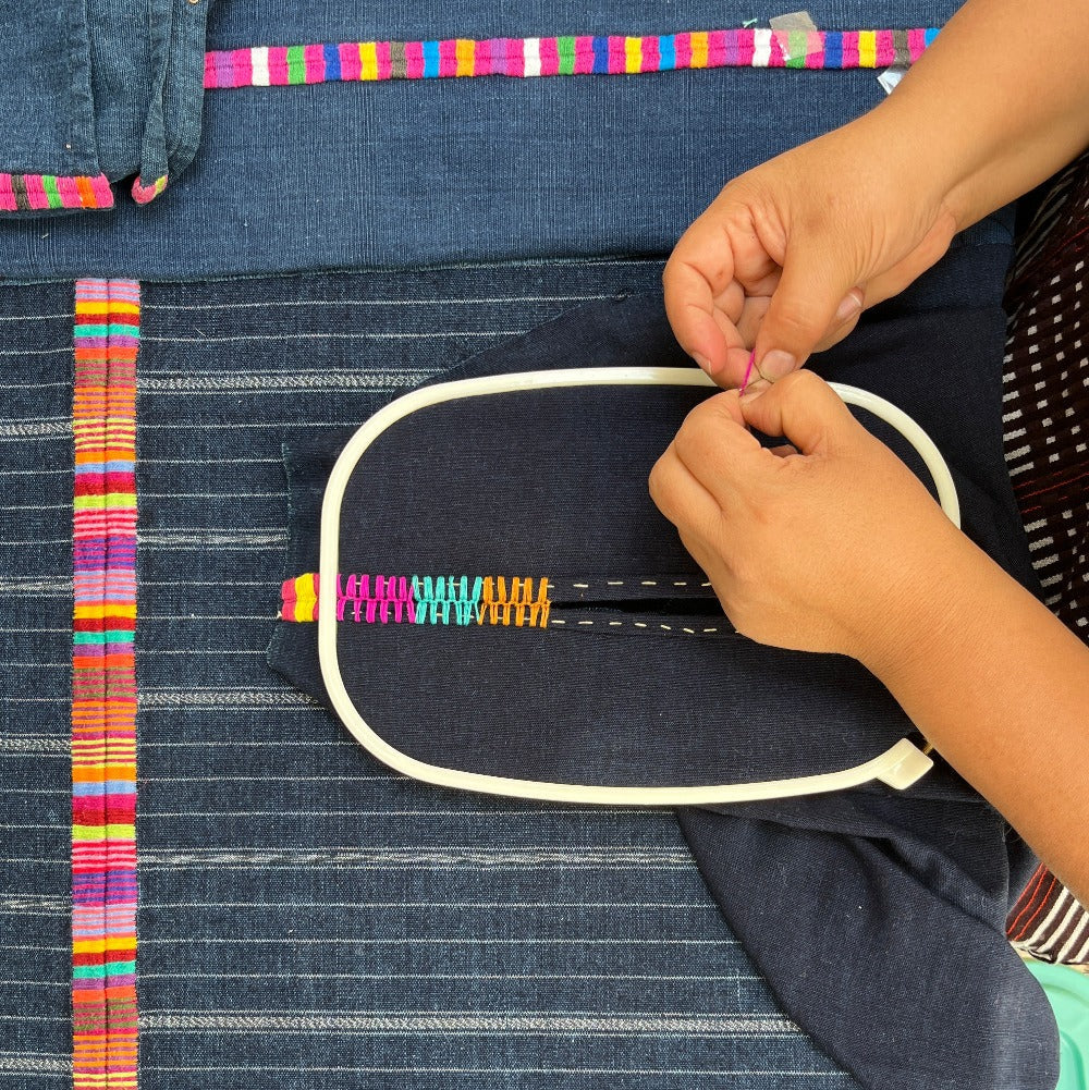 Birds-eye view of hands working colorful stitches on indigo blue fabric.