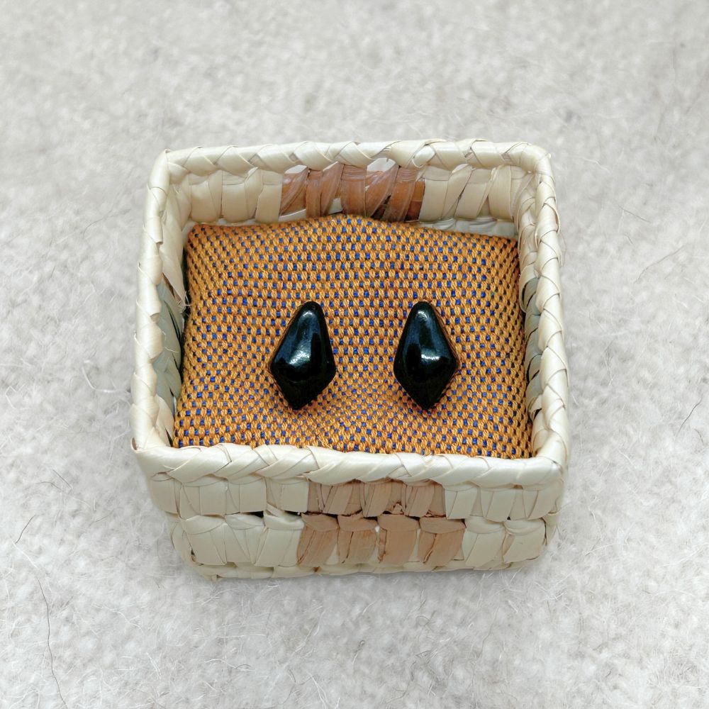 Rhombus-Shaped Black Jade Stud Earrings in a woven palm basket on a textured surface