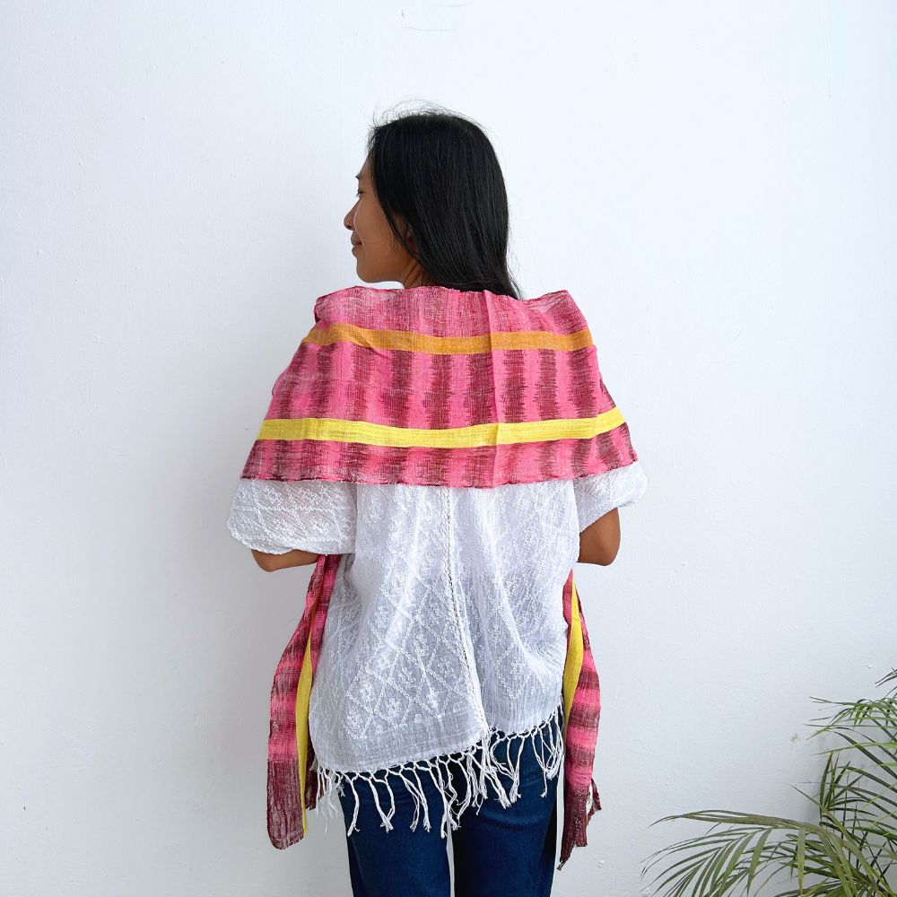 Person wearing a colorful striped shawl over a white top and blue jeans against a white background.