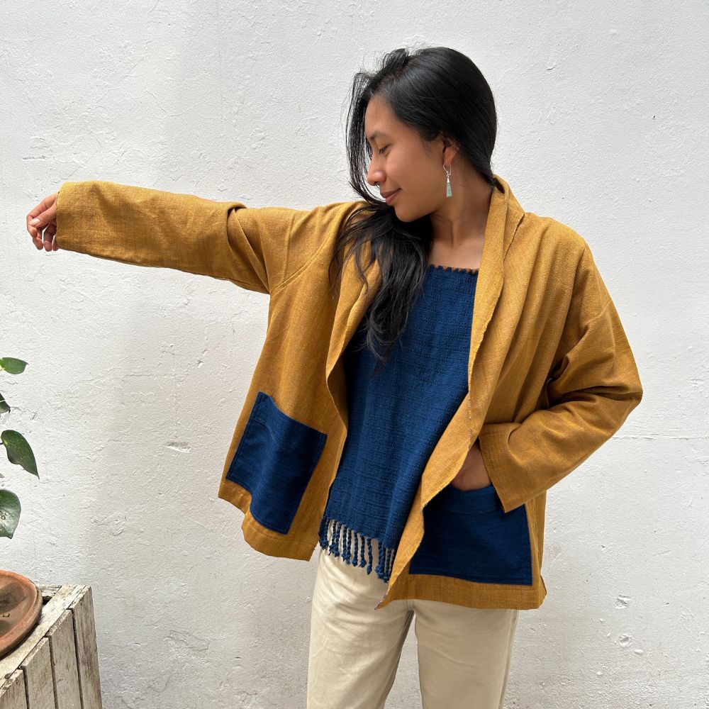 A person wearing a cardigan with one sleeve extended to show the inside. The cardigan has a mix of mustard yellow and blue colors.