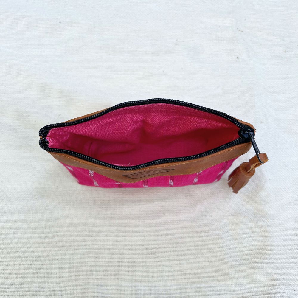 An open zippered pouch with a bright pink patterned exterior, a vivid pink interior, and brown leather trim, shown on a light beige fabric background.