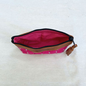 An open zippered pouch with a bright pink patterned exterior, a vivid pink interior, and brown leather trim, shown on a light beige fabric background.