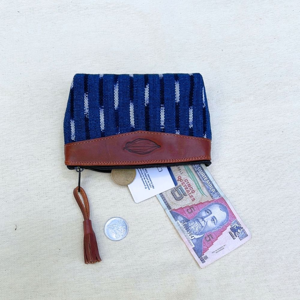 A woven pouch in navy blue and white with a brown leather trim and tassel, shown open with a coin, card, and banknote inside on a light fabric background.
