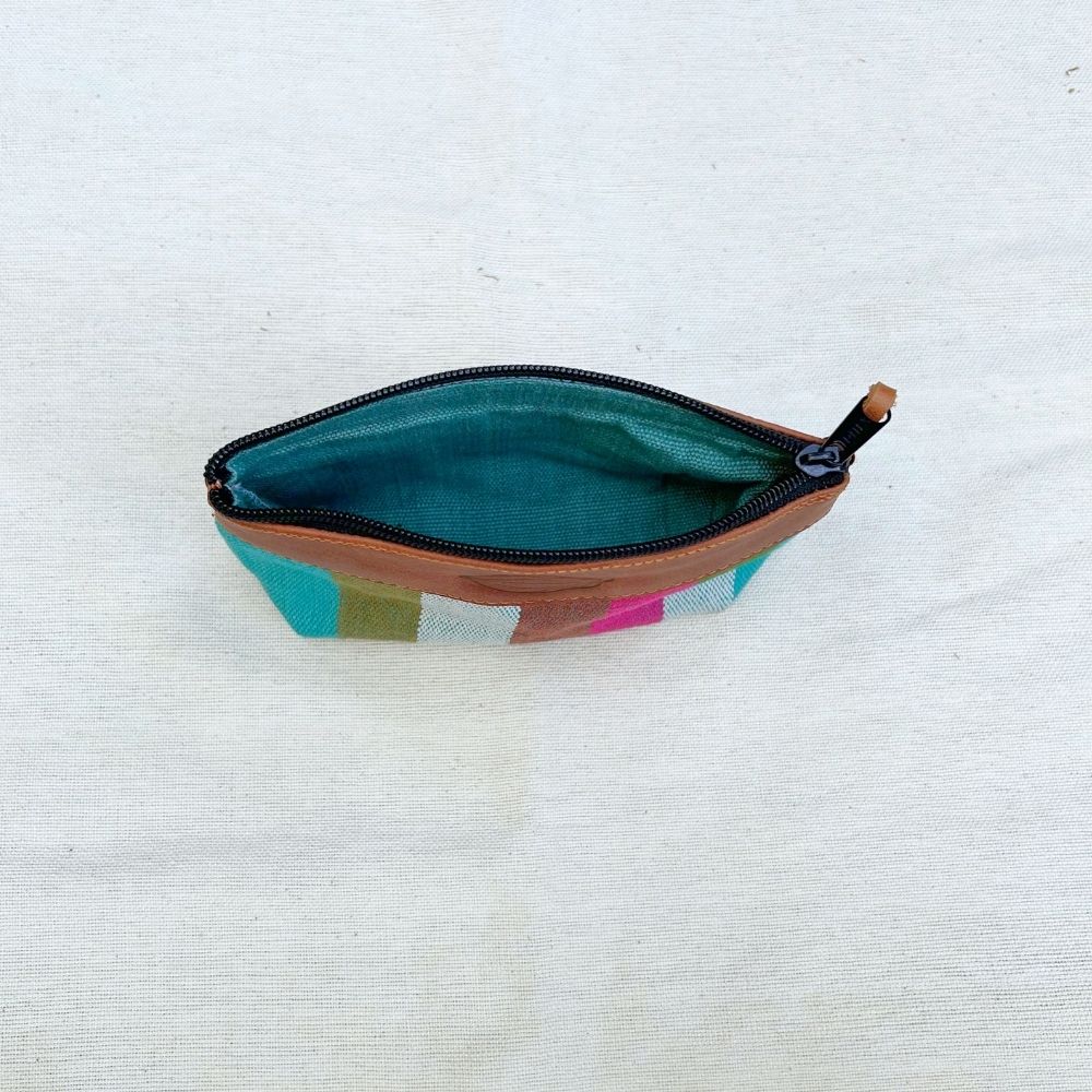 A zippered pouch with a brown leather trim, a teal interior lining, and a multicolor geometric pattern on the exterior, shown open on a light beige fabric background.