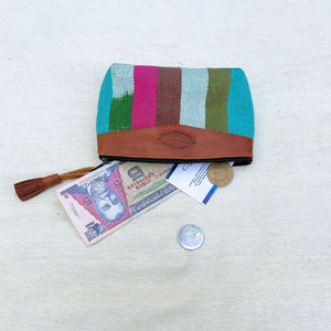 A woven pouch with a multicolor striped pattern and a brown leather top band, shown open with cash and coins beside it on a light fabric background.