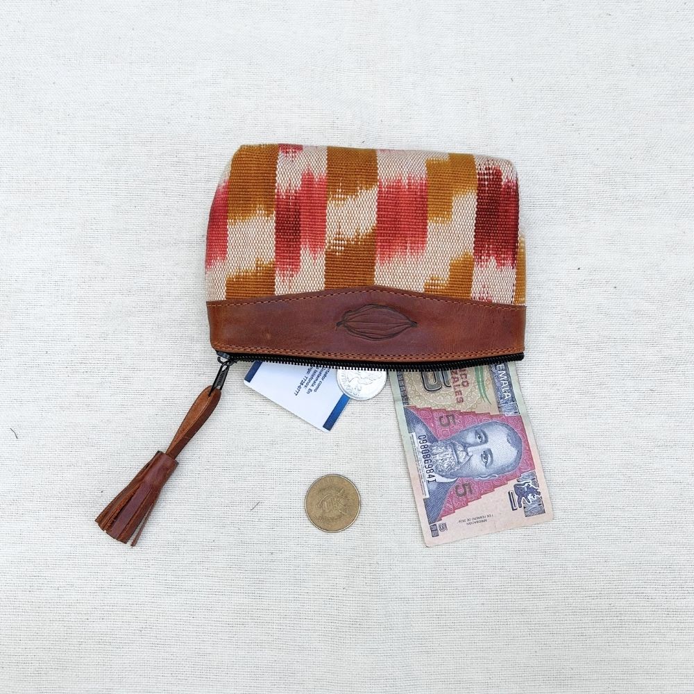 A zippered pouch with a brown leather top panel and a woven body featuring vertical stripes in orange, red, and beige. A tassel hangs from the zipper.