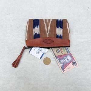 A woven zippered pouch with a brown leather trim and tassel, shown open with a banknote, coin, and card peeking out on a light textured fabric background.