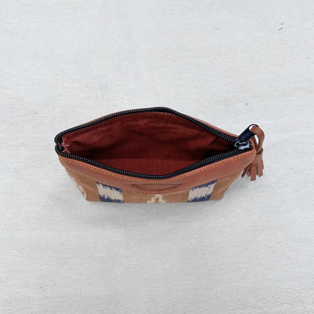 A zippered pouch with a brown leather top and tassel, featuring a geometric pattern in blue, white, and brown on the exterior, and a light coffee interior lining, shown on a light textured fabric background.