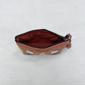 A zippered pouch with a brown leather top and tassel, featuring a geometric pattern in blue, white, and brown on the exterior, and a light coffee interior lining, shown on a light textured fabric background.