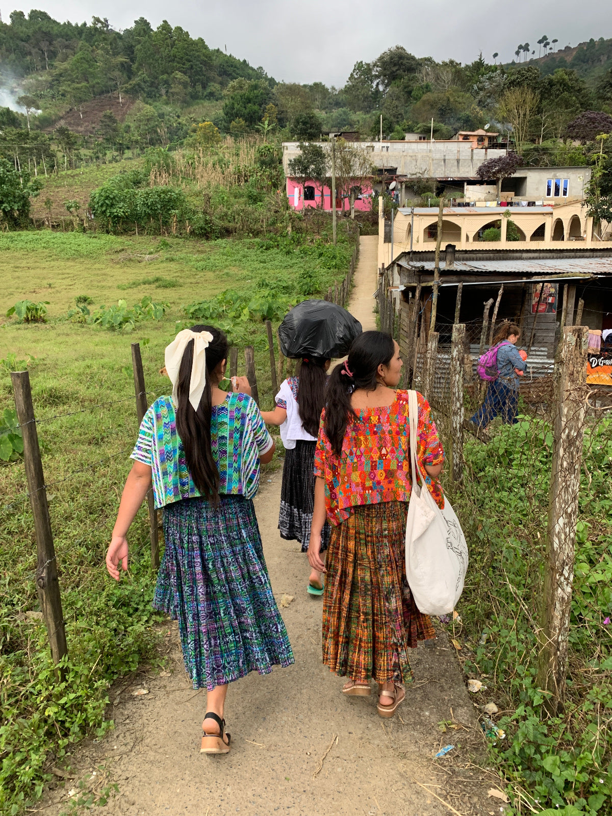 Girls walking through a narrow path in a rural village wearing colorful traditional garments.