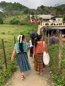 Girls walking through a narrow path in a rural village wearing colorful traditional garments.