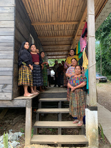 Group of women in traditional clothing standing on a wooden platform.