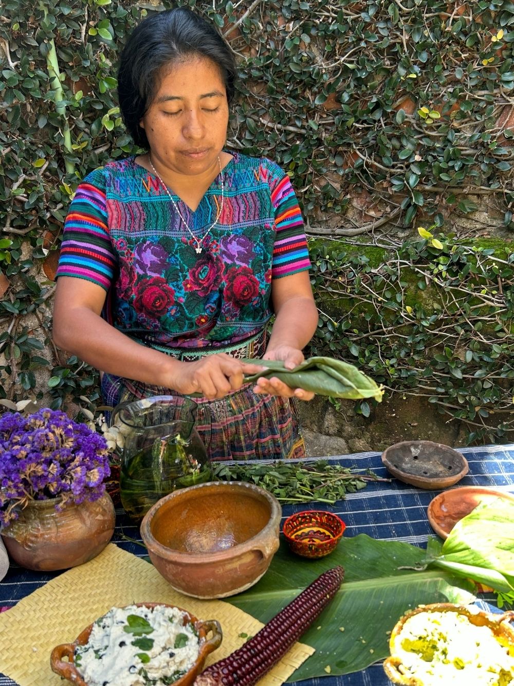 Woman in traditional clothing preparing food outdoors with a table full of ingredients.