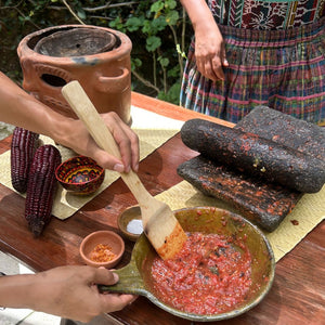 Person preparing food with traditional tools and ingredients on a wooden table.