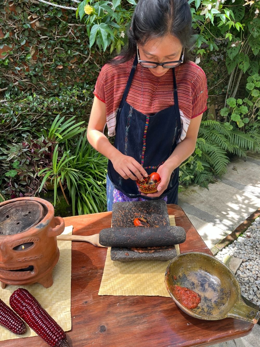 Person preparing food outdoors with a mortar and pestle, surrounded by greenery.