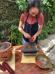 Person preparing food outdoors with a mortar and pestle, surrounded by greenery.