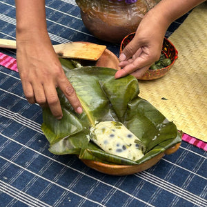 Person wrapping a tamal in maxan leaves on a blue striped surface